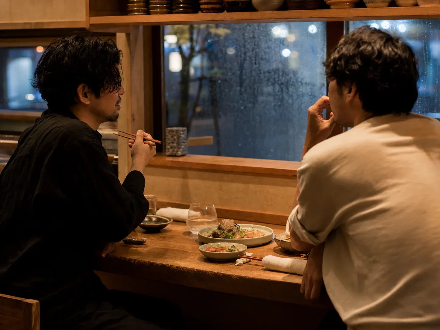 Friends sharing a quiet meal in a small izakaya on a rainy evening