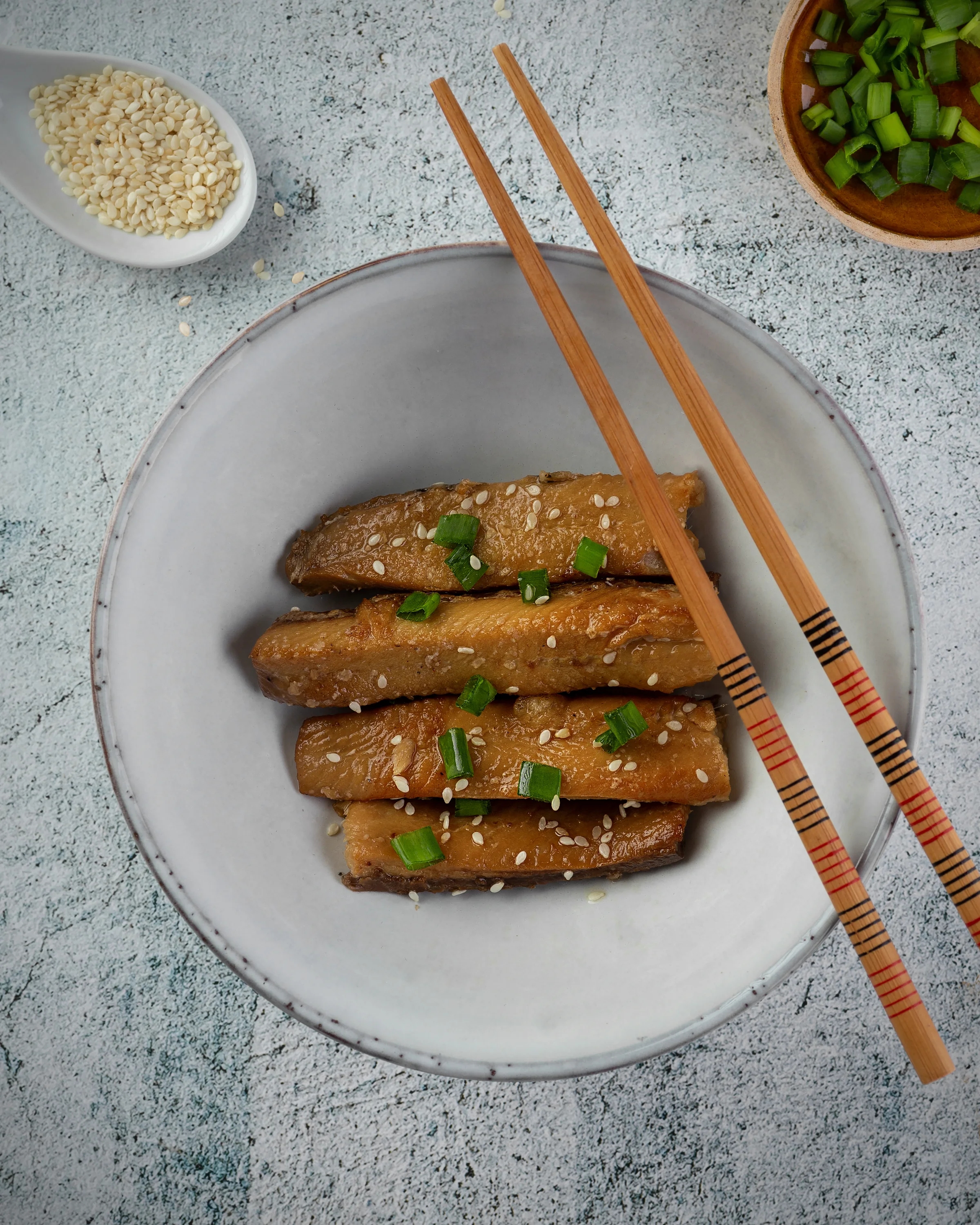 Glazed fish pieces served with sesame seeds and spring onion in a ceramic bowl