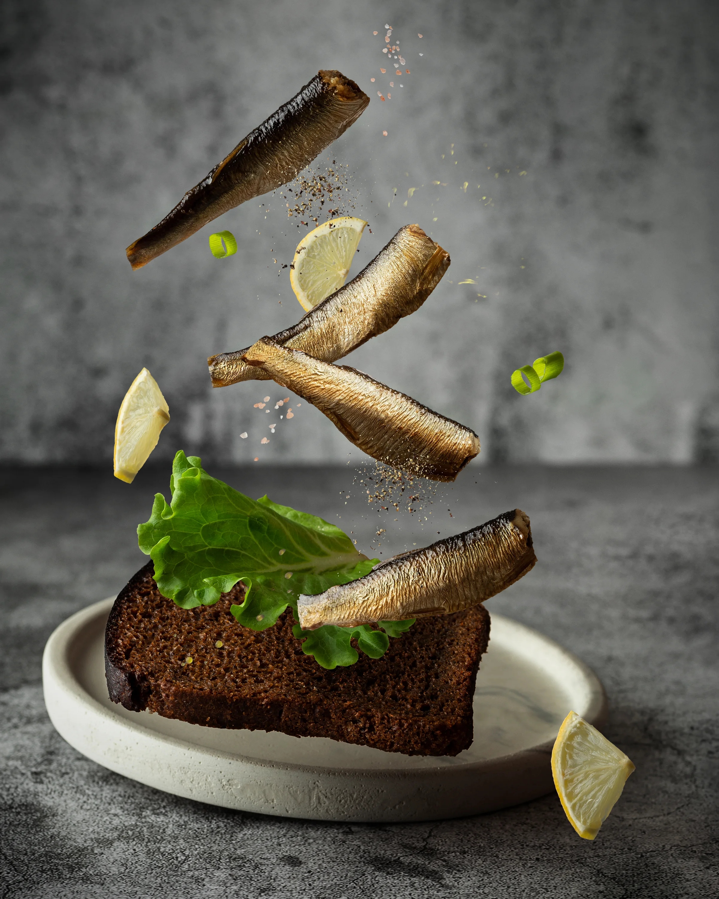 Smoked sprats arranged above rye bread with lettuce, lemon and seasoning
