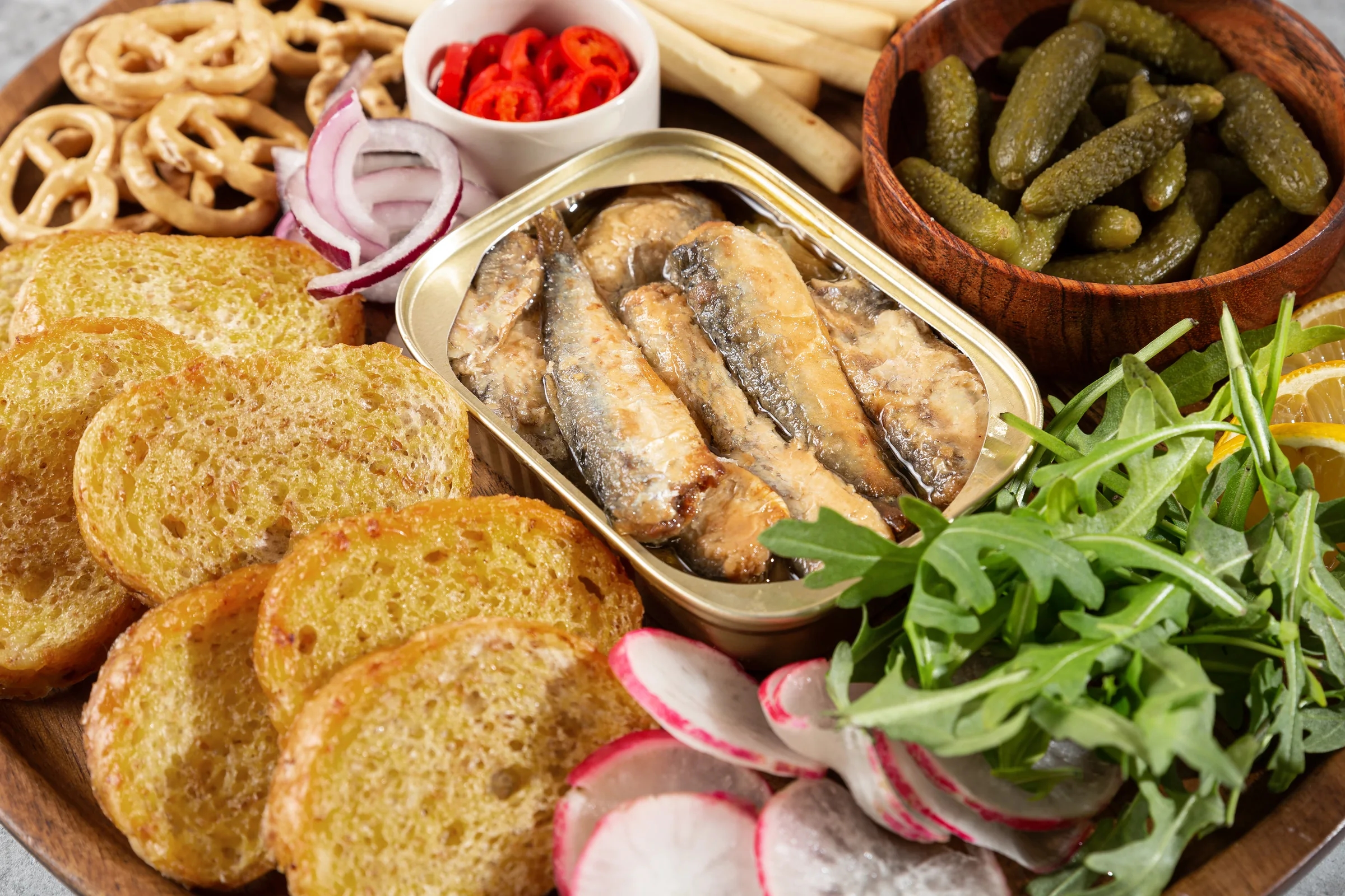 An open tin of sardines served with toasted bread, pickles, red onion, radishes and rocket