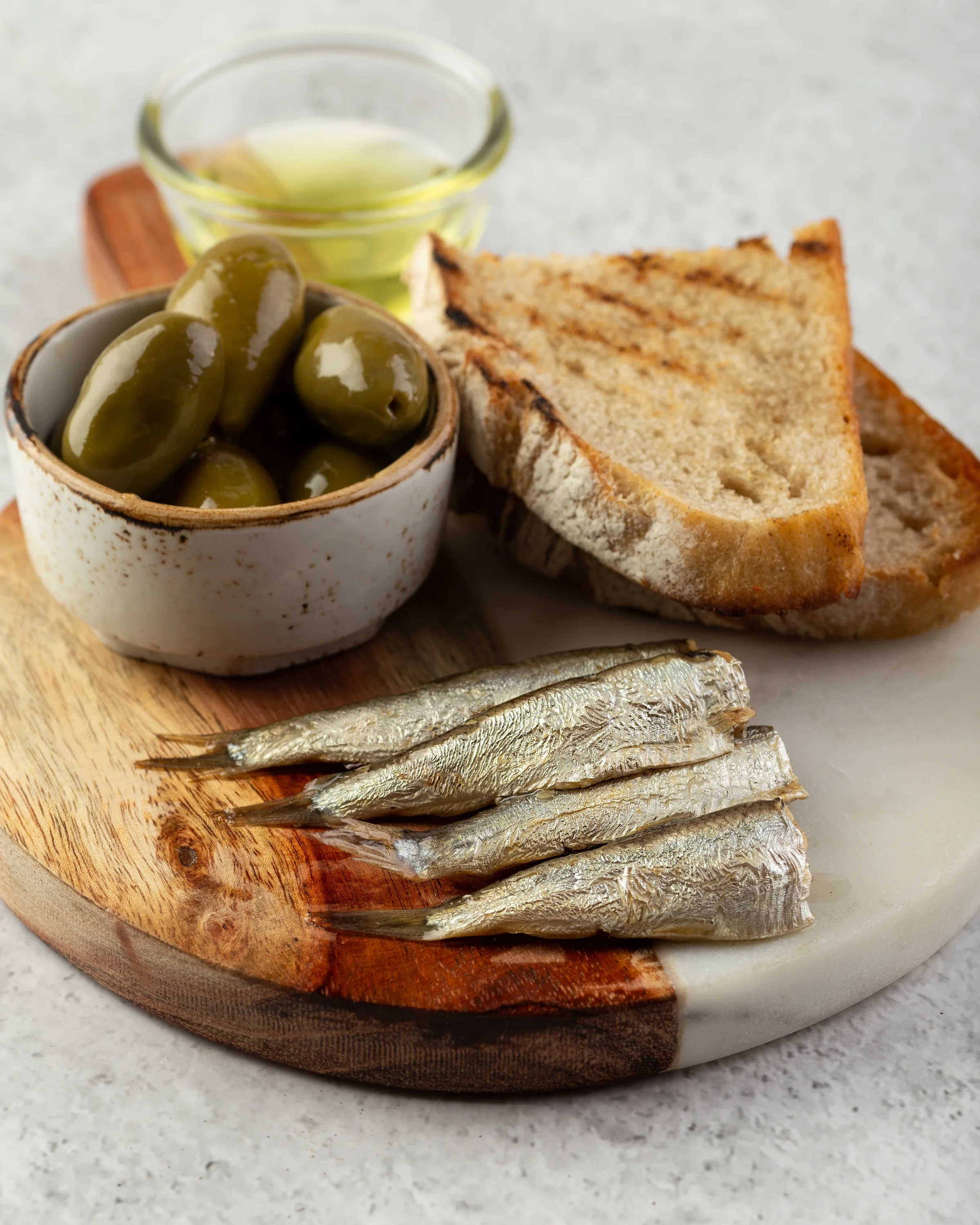 Smoked sprats served with grilled bread, green olives and olive oil