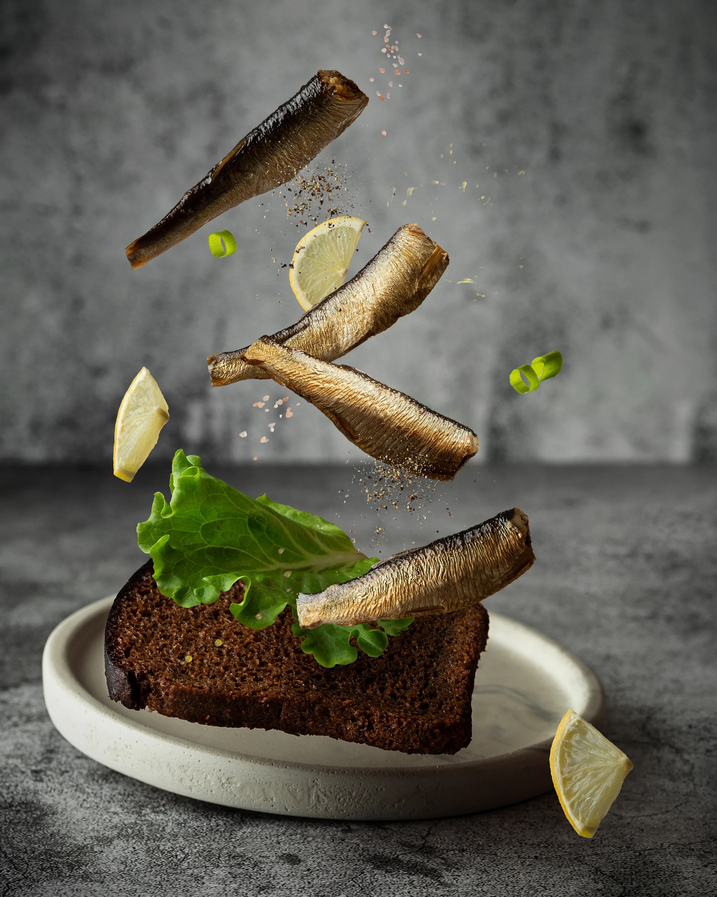 Smoked sprats arranged above rye bread with lettuce, lemon and seasoning