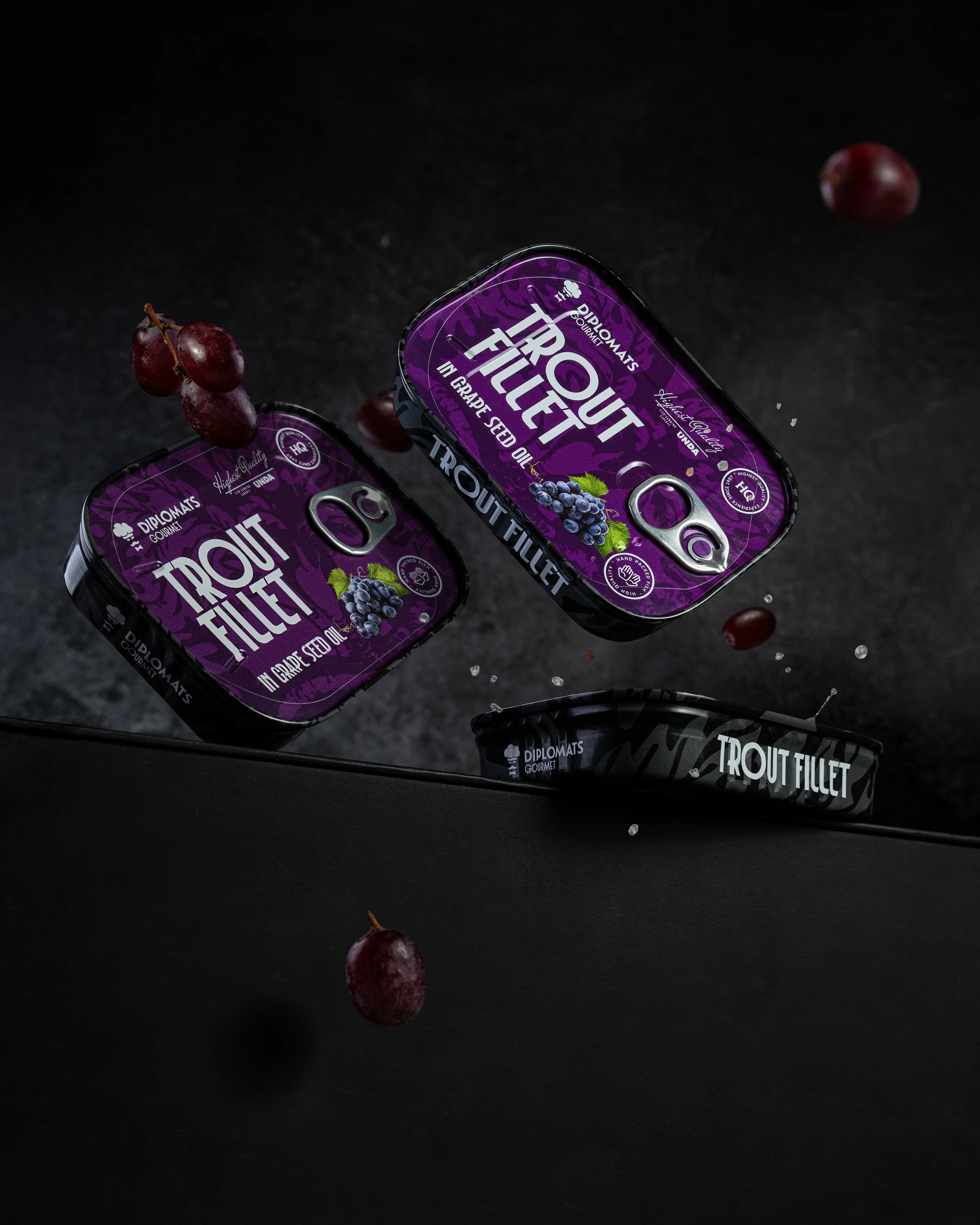 Diplomats trout fillet tins with grape-seed oil and grapes in a dark campaign composition